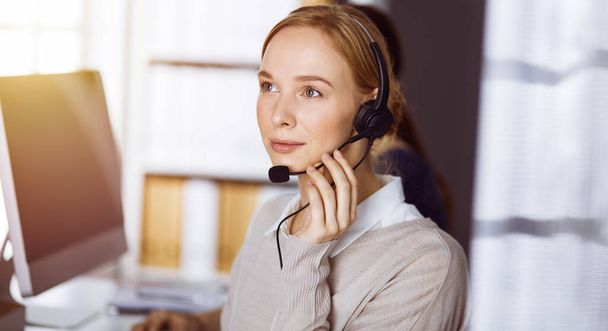 Businesswoman talking by headset in sunny office. Call center and diverse people group in business - Photo, Image