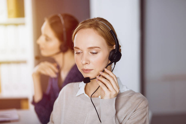 Businesswoman talking by headset in sunny office. Call center and diverse people group in business - Foto, afbeelding