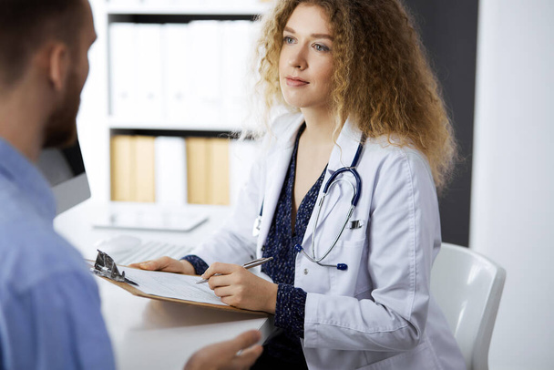 Female doctor and male patient discussing current health examination while sitting in clinic. Perfect medical service and medicine concept - Foto, afbeelding