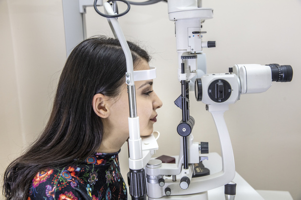 Hoogtechnologische concept gezondheid voor oogverzorging - De opticien oogarts optometrist in de oogkliniek met behulp van een binoculaire spleetlamp voor een jonge vrouw voor een oogcontrole.  - Foto, afbeelding