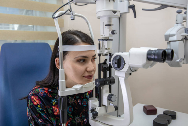 Hoogtechnologische concept gezondheid voor oogverzorging - De opticien oogarts optometrist in de oogkliniek met behulp van een binoculaire spleetlamp voor een jonge vrouw voor een oogcontrole.  - Foto, afbeelding