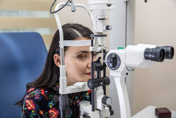 Υψηλή τεχνολογία έννοια της υγείας για τη φροντίδα των ματιών - Ο οφθαλμίατρος οφθαλμίατρος οφθαλμίατρος οφθαλμίατρος στην κλινική ματιών χρησιμοποιώντας μια διόφθαλμη σχισμή-λάμπα σε μια νεαρή γυναίκα για τον έλεγχο των ματιών.  - Φωτογραφία, εικόνα
