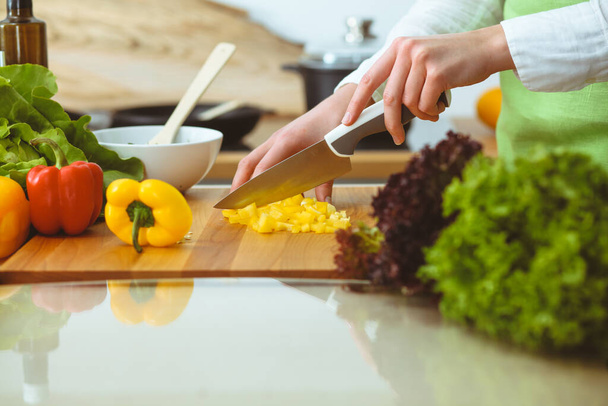 Unknown human hands cooking in kitchen. Woman slicing yellow bell pepper. Healthy meal, and vegetarian food concept - 写真・画像