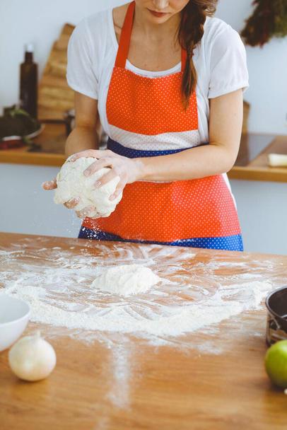Young brunette woman cooking pizza or handmade pasta in the kitchen. Housewife preparing dough on wooden table. Dieting, food and health concept - Zdjęcie, obraz