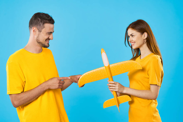 Joven pareja hermosa jugando con el avión de juguete amarillo en fondo azul  - Foto, imagen
