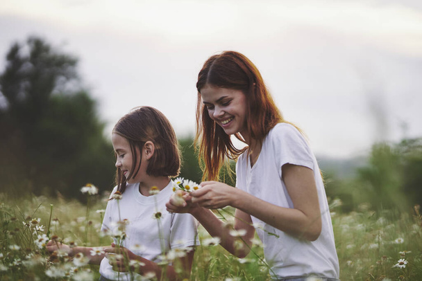 Young mother and her daughter having fun on camomile field - Foto, imagen