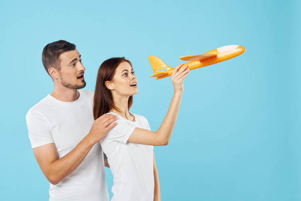 Young beautiful couple playing with yellow toy plane on blue background  - Photo, Image