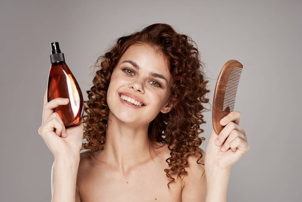 Young beautiful woman with curly hair holding hair spray and wooden comb. Studio shot - Fotoğraf, Görsel