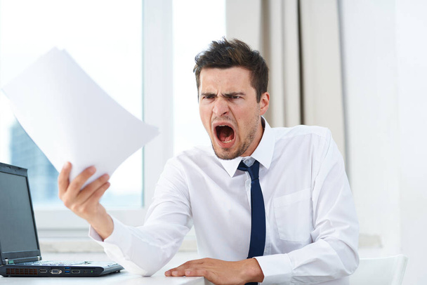 Jeune homme d'affaires en colère dans le bureau avec des papiers  - Photo, image