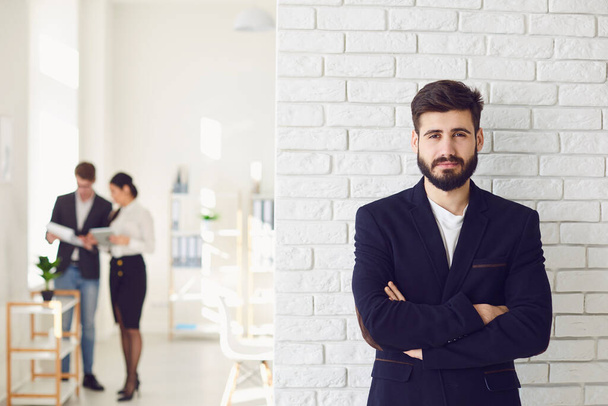 Positive happy bearded businessman in a jacket smiling while standing against a white office background. - Foto, imagen