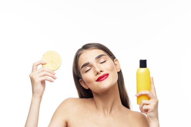 Jonge mooie vrouw die haar gezicht schoonmaakt met spons. Schoonheidsroutine. Studioshoot - Foto, afbeelding