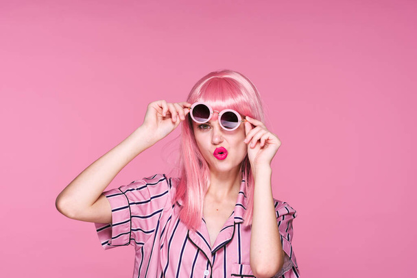 νεαρή όμορφη γυναίκα με ροζ περούκα και γυαλιά ηλίου ποζάρουν στο στούντιο  - Φωτογραφία, εικόνα