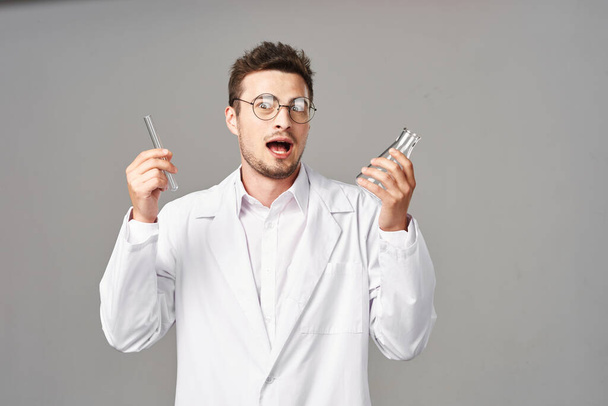 sorprendido Doctor en bata de laboratorio con tubos de ensayo sobre fondo gris. Captura de estudio - Foto, Imagen