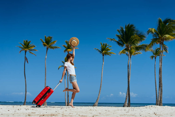  Junge Frau mit rotem Koffer am Strand - Foto, Bild