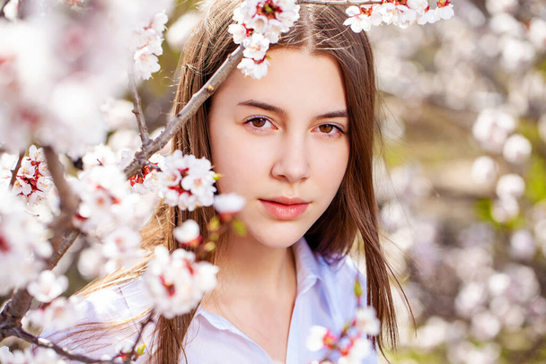 Pretty teen girl are posing in garden near blossom cherry tree with white flowers. Spring time  - Zdjęcie, obraz