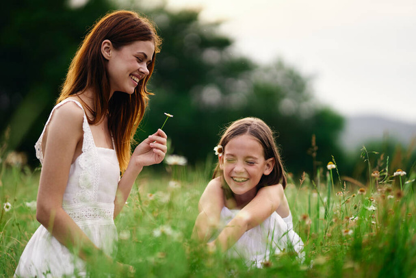 Young mother and her daughter having fun on camomile field - Foto, imagen