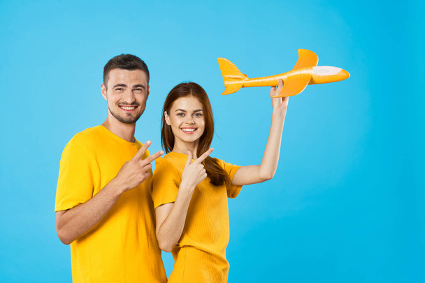 Young beautiful couple playing with yellow toy plane on blue background  - Foto, Bild