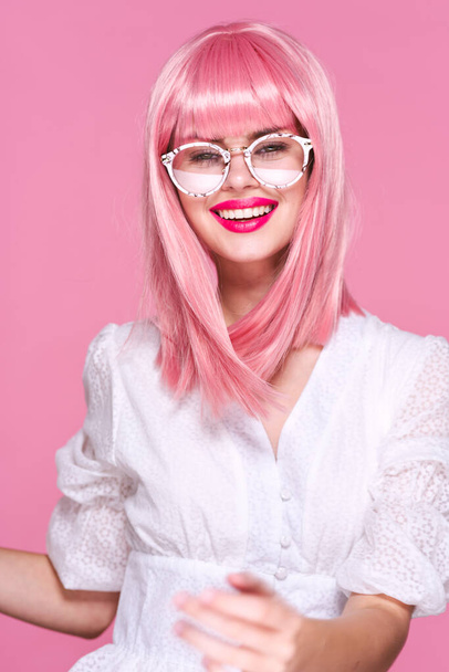 Jeune femme en perruque rose et lunettes sur fond rose - Photo, image