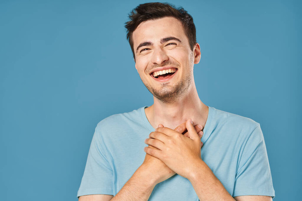 νεαρός όμορφος άντρας χαμογελάει στο στούντιο σε μπλε φόντο  - Φωτογραφία, εικόνα