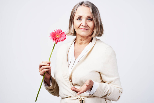 Mooie senior vrouw met roze bloem in studio - Foto, afbeelding