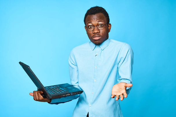 Young african surprised  businessman holding laptop isolated on blue background - Zdjęcie, obraz