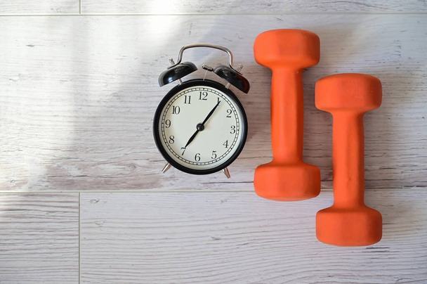 Top view on a pair of orange dumbbell and alarm clock. The concept of doing sports early in the morning. Time for self-training at home. - Photo, Image