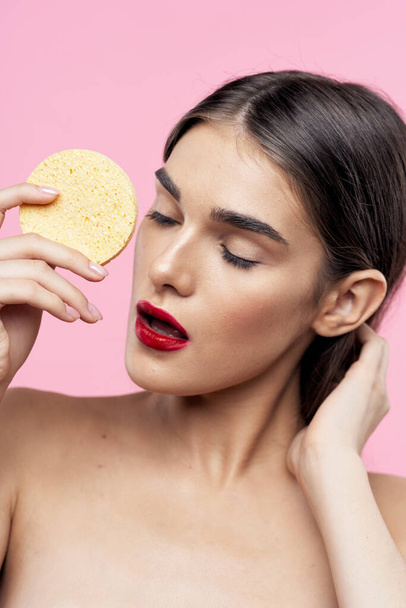 Cuidado de la piel y belleza. Retrato de una joven hermosa mujer limpiando su piel con esponja sobre fondo rosa
 - Foto, imagen