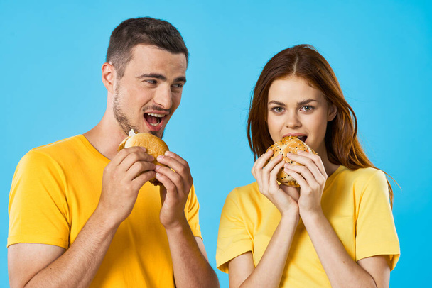 スタジオでハンバーガーを食べる若い美しい空腹のカップル。隔離。 - 写真・画像