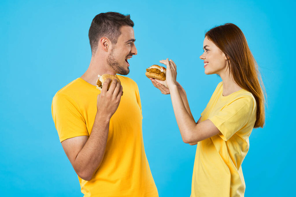 Молодая красивая пара ест гамбургеры. Снимок студии - Фото, изображение