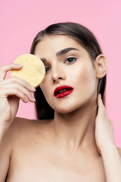 Skincare and beauty. Portrait of young beautiful woman cleaning her skin with sponge on pink background - Photo, Image