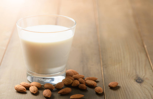 木の背景に牛乳やアーモンドナッツのガラス、アーモンドは非常に人気のナッツや高タンパク質です。健康食品. - 写真・画像