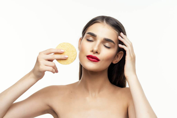 Young beautiful woman cleaning her face with sponge. Beauty routine. Studio shot - Foto, Bild