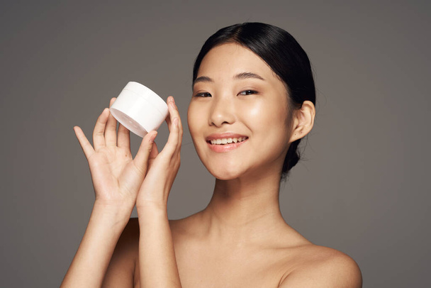 Студийный снимок Молодая азиатка держит крем на сером
   - Фото, изображение