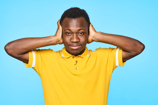 青い背景に隔離された耳を閉じる若いアフリカ人男性 - 写真・画像