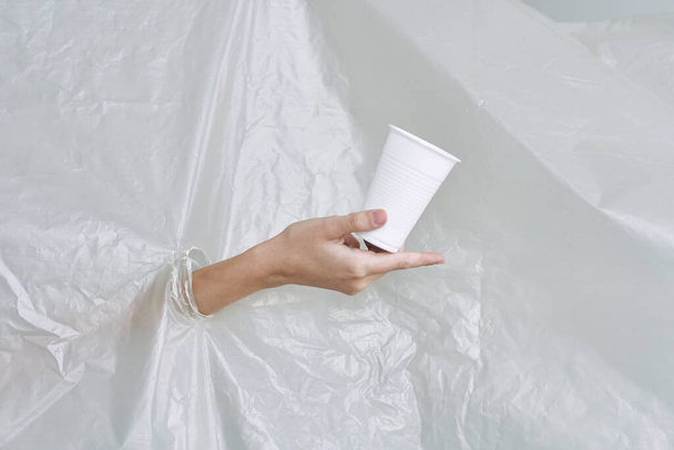 female hand with cup   tearing plastic, polyethylene - Fotografie, Obrázek