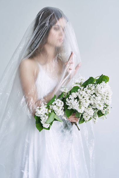 Jeune femme sous bâches en plastique tenant des fleurs. Concept d'écologie - Photo, image
