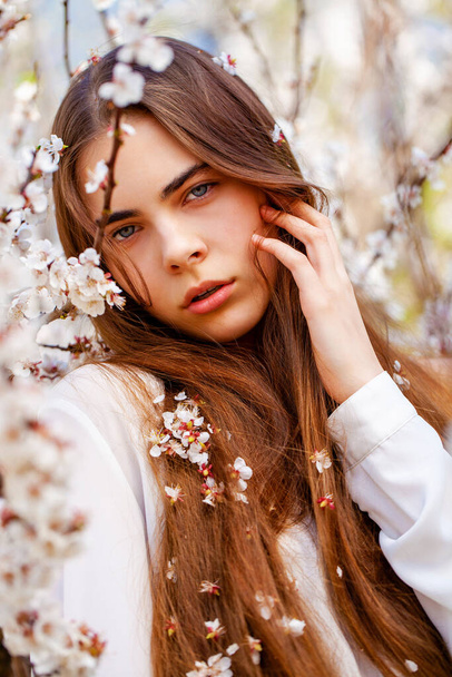 Pretty teen girl are posing in garden near blossom cherry tree with white flowers. Spring time  - Foto, immagini