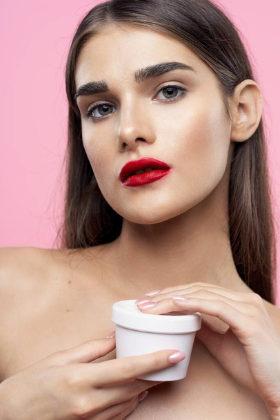 Hautpflege und Schönheit. Porträt einer jungen schönen Frau mit Creme auf rosa Hintergrund - Foto, Bild