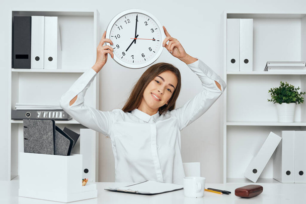 Young businesswoman sitting at desk in the office with clock - Фото, зображення
