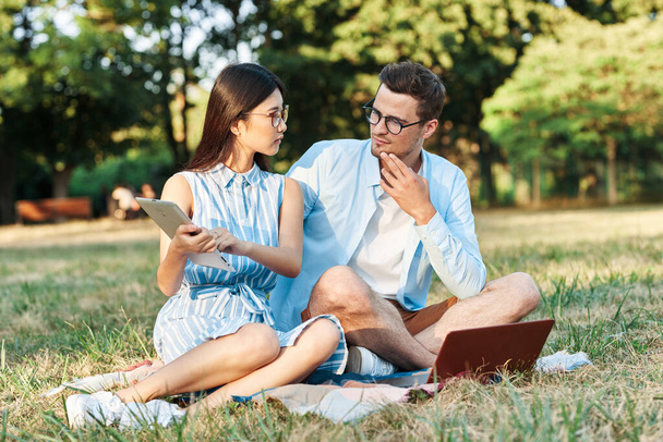 jeunes étudiants avec ordinateur portable et tablette assis sur la pelouse  - Photo, image