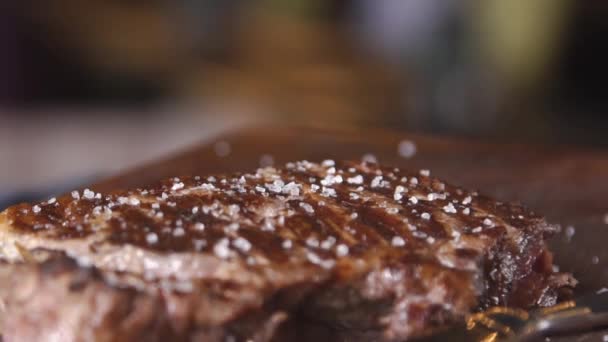 Meat steak. Meat and rosemary. A close up of a steak with sea salt and herbs. Steak on a wooden board in a restaurant.  Serving a steak at a meat restaurant. - Materiał filmowy, wideo