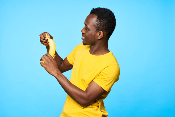 Giovane uomo africano con banana isolato su sfondo blu - Foto, immagini