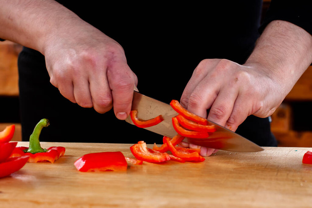 the cook slices red peppers on a wooden Board - 写真・画像