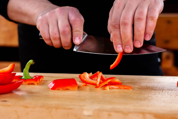 the cook slices red peppers on a wooden Board - Foto, Bild