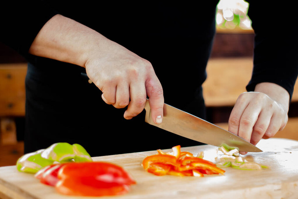 the cook cuts green peppers into strips on a wooden Board - Foto, afbeelding