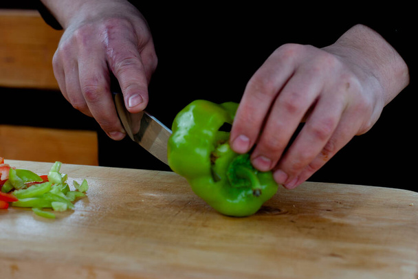 the cook cuts green peppers into strips on a wooden Board - 写真・画像