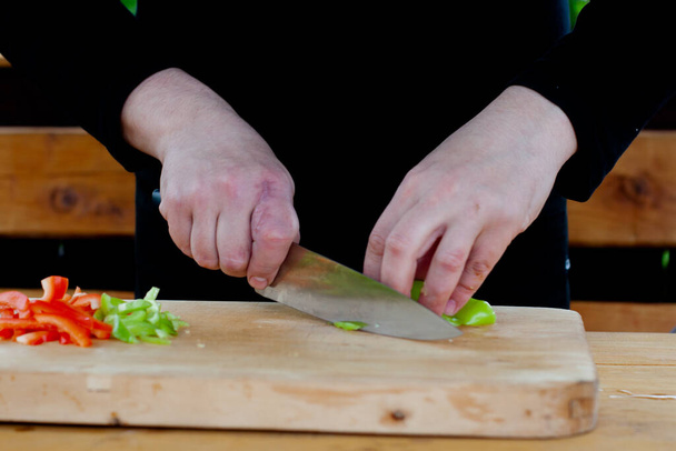 the cook cuts green peppers into strips on a wooden Board - Fotó, kép
