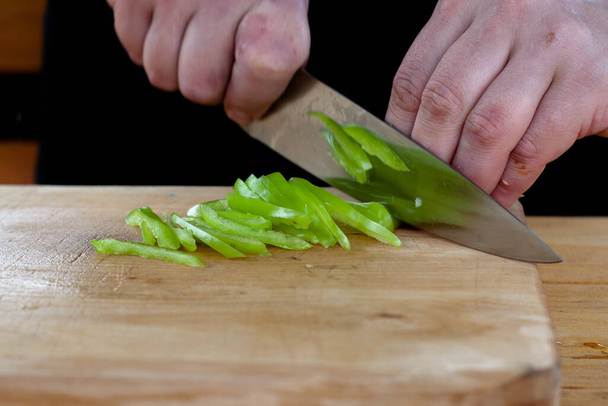 the cook cuts green peppers into strips on a wooden Board - Fotó, kép