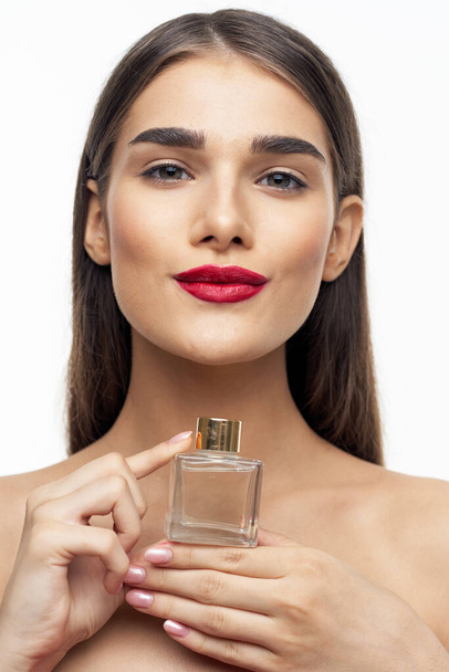 Young beautiful woman holding perfume bottle in studio - Foto, imagen