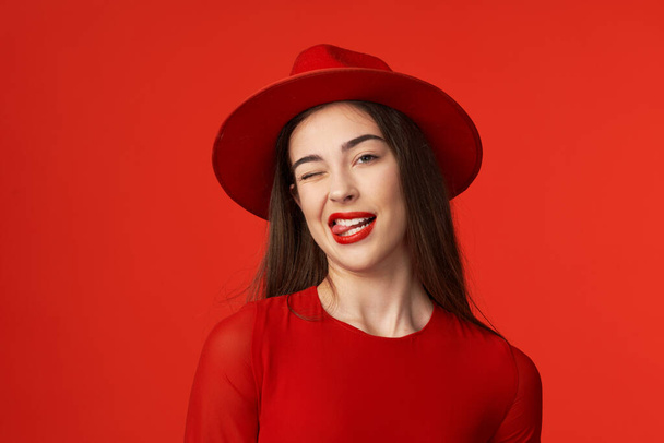 Studio shot. Young beautiful woman in red winking  isolated on red background - Photo, Image